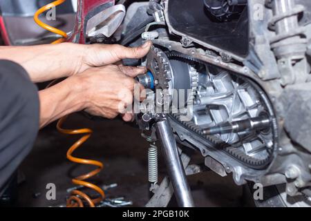 Il meccanico della motocicletta controlla le condizioni del sistema di trasmissione automatica o del sistema della frizione dello scooter in officina. Concetto di riparazione e manutenzione della motocicletta Foto Stock