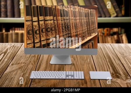 Biblioteca online. Computer moderno su tavolo di legno e scaffali con libri al coperto Foto Stock