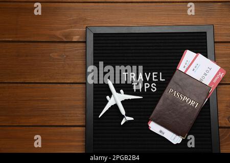 Lavagna a lettere nera con la frase Consigli di viaggio, passaporto, biglietti e aereo giocattolo su un tavolo di legno, vista dall'alto. Spazio per il testo Foto Stock