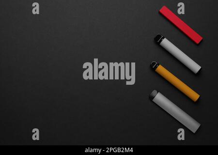 Dispositivi elettronici monouso per fumare su sfondo nero, a posa piatta. Spazio per il testo Foto Stock