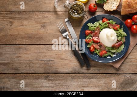 Deliziosa insalata di burrata con pomodori, prosciutto e rucola servita su tavolo di legno, piatto. Spazio per il testo Foto Stock