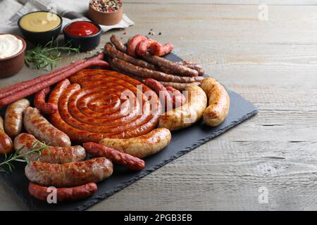 Diverse e deliziose salsicce con rosmarino e salse su tavola in legno. Assortimento di spuntini alla birra Foto Stock