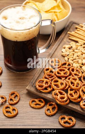 Bicchiere di birra servito con deliziosi cracker di pretzel e altri spuntini sul tavolo di legno Foto Stock