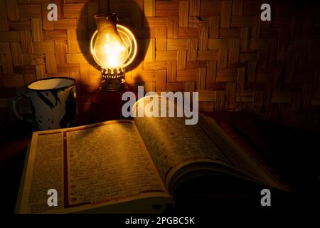 Il Santo Corano sul tavolo di legno con lampada tradizionale di kerosene vintage e bambù intrecciato come sfondo. Scatto da studio con esposizione lunga. Sfocato. Foto Stock