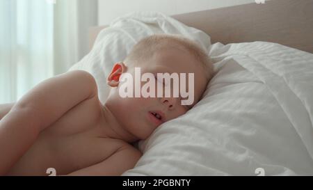 Un bambino tranquillo e spensierato che dorme sul letto della camera. 4k concetto di suono e di sonno sano del bambino. Assistenza ai bambini. Buona infanzia. Foto Stock