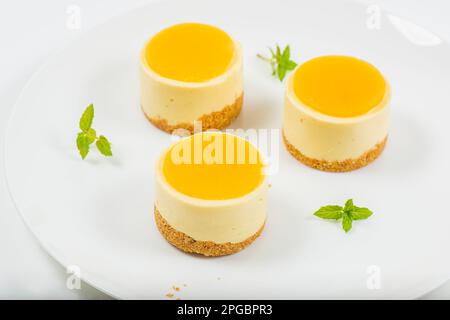 Cheesecake cremoso al mango piccolo con gelatina di mango e una base di briciole di grano integrale. Foto Stock