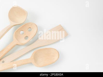 Utensili da cucina in legno. Cucchiai, spatola e paletta di legno giacono diagonalmente su uno sfondo bianco a specchio Foto Stock