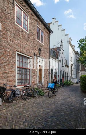 La giovane donna va in bici con la sua borsa della spesa attraverso una strada medievale ad Amersfoort. Foto Stock
