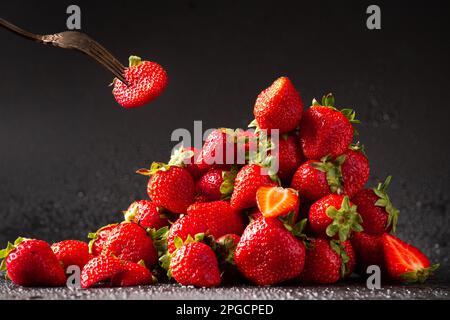 Una collina di fragola rossa con gocce d'acqua su uno sfondo scuro primo piano. Prodotto dietetico utile. Foto Stock