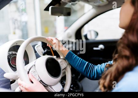 Vista laterale di una giovane conducente femminile dal taglio irriconoscibile in un'auto da guida dolcevita con interni bianchi Foto Stock