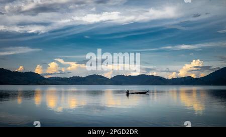 Un uomo di minoranza etnica di Mnong solitario sulla sua canoa di legno si dirige a pescare sul lago Lak a buon Jun a Lien Son, Vietnam. Foto Stock