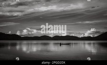 Un uomo di minoranza etnica di Mnong solitario sulla sua canoa di legno si dirige a pescare sul lago Lak a buon Jun a Lien Son, Vietnam. Foto Stock