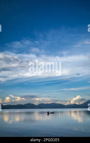 Un uomo di minoranza etnica di Mnong solitario sulla sua canoa di legno si dirige a pescare sul lago Lak a buon Jun a Lien Son, Vietnam. Foto Stock