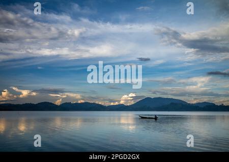 Un uomo di minoranza etnica di Mnong solitario sulla sua canoa di legno si dirige a pescare sul lago Lak a buon Jun a Lien Son, Vietnam. Foto Stock