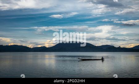 Un uomo di minoranza etnica di Mnong solitario sulla sua canoa di legno si dirige a pescare sul lago Lak a buon Jun a Lien Son, Vietnam. Foto Stock