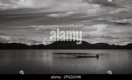 Un uomo di minoranza etnica di Mnong solitario sulla sua canoa di legno si dirige a pescare sul lago Lak a buon Jun a Lien Son, Vietnam. Foto Stock