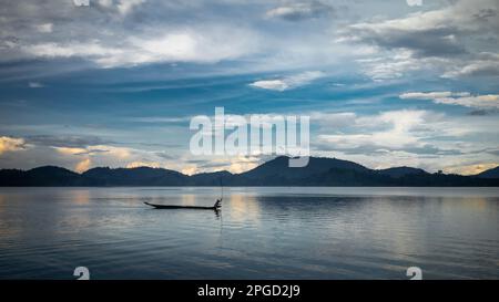 Un uomo di minoranza etnica di Mnong solitario sulla sua canoa di legno getta la sua canna da pesca nel lago Lak a buon Jun a Lien Son, Vietnam. Foto Stock