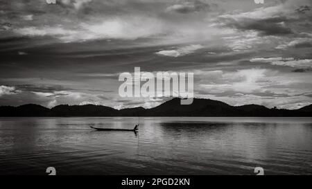 Un uomo di minoranza etnica di Mnong solitario sulla sua canoa di legno getta la sua canna da pesca nel lago Lak a buon Jun a Lien Son, Vietnam. Foto Stock