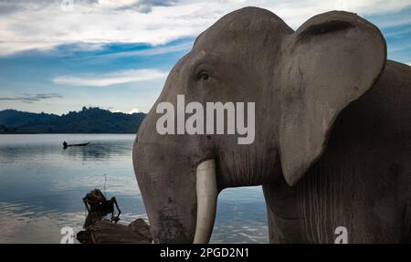 Un grande elefante di cemento è guardia al bordo del lago Lak, a buon Jun, Lien Son, Vietnam. Gli elefanti sono addestrati e di proprietà del locale Mnong eth Foto Stock