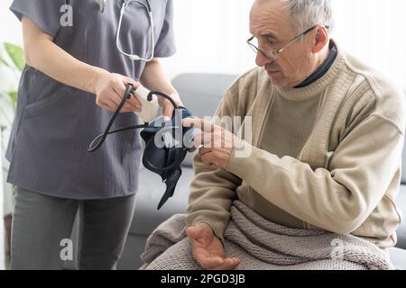 Giovane infermiera sorridente che prende la pressione sanguigna del vecchio Foto Stock