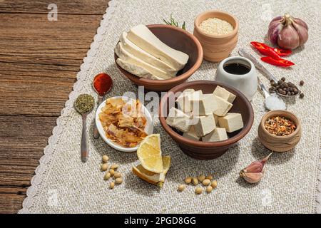 Set di ingredienti per la preparazione tofu. Formaggio fresco a dadini, spezie, erbe aromatiche e salsa di soia. Trendy luce dura, ombra scura, sfondo in legno vintage, c Foto Stock