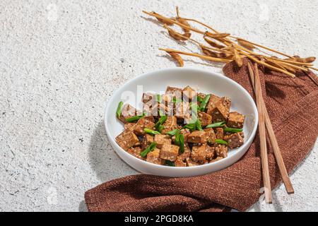 Tofu teriyaki fritto con scalioni e semi di sesamo. Pasto vegano sano senza carne ricco di proteine e calcio. Luce dura alla moda, ombra scura, intonaco Foto Stock