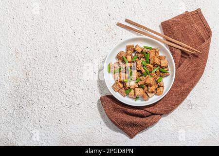 Tofu teriyaki fritto con scalioni e semi di sesamo. Pasto vegano sano senza carne ricco di proteine e calcio. Luce dura alla moda, ombra scura, intonaco Foto Stock