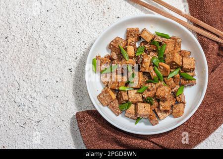 Tofu teriyaki fritto con scalioni e semi di sesamo. Pasto vegano sano senza carne ricco di proteine e calcio. Luce dura alla moda, ombra scura, intonaco Foto Stock