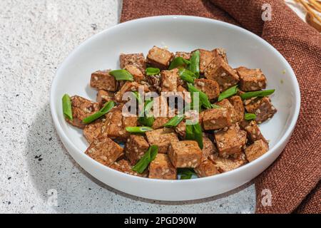 Tofu teriyaki fritto con scalioni e semi di sesamo. Pasto vegano sano senza carne ricco di proteine e calcio. Luce dura alla moda, ombra scura, intonaco Foto Stock