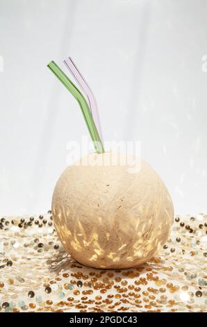 Bevanda all'acqua di cocco con 2 cannucce di vetro per una festa. Succo di cocco fresco su uno sfondo scintillante Foto Stock