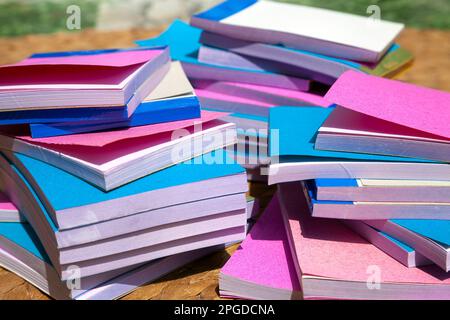 Molti piccoli notepads economici in 3 pile disordinato visto da un lato. Un mucchio di semplici graffette blu e rosa impilate sul pavimento Foto Stock