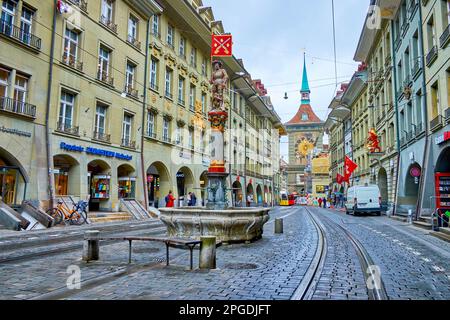 BERNA, SVIZZERA - 31 MARZO 2022: Via Marktgasse con fontana medievale Schutzenbrunnen e torre Zytglogge sullo sfondo, il 31 marzo a Berna, S. Foto Stock