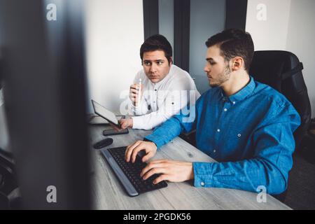 Due giovani programmatori caucasici che lavorano su computer desktop in ufficio per lo sviluppo di un nuovo videogioco Foto Stock