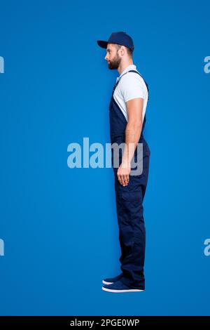 Profilo del corpo full-size verticale, scatto di attraente, sicuro offrire in blu uniforme con barba corta, isolato su sfondo grigio Foto Stock