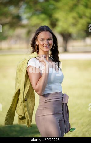 Foto di una bella giovane donna nei suoi primi anni '30s in posa all'aperto con giacca appesa al braccio Foto Stock