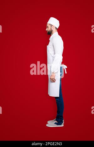 Profilo vista laterale snap, corpo ritratto a grandezza naturale di bella macellaio attraente isolato su sfondo grigio, indossando camicia bianca, grembiule, jeans Foto Stock