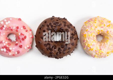 Tre ciambelle in fila - bianco, rosa e cioccolato su uno sfondo bianco vista dall'alto Foto Stock