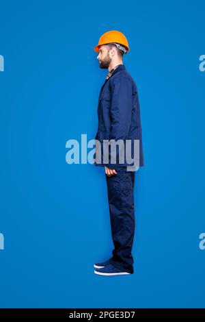 Bottoncino full-body con gambe, profilo ritratto di un bel riparatore calmo in uniforme blu, isolato su sfondo grigio Foto Stock