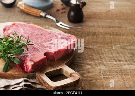 Bistecca con osso a T crudo spesso. Carne di manzo cruda e invecchiata a secco con erbe e sale su fondo scuro. Messa a fuoco selettiva e spazio di copia. Foto Stock