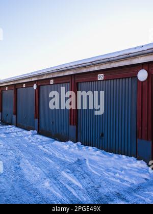 File di coloratissimi garage in Svezia, ricoperti dalla fresca nevicata in una fredda giornata invernale sotto il cielo azzurro. Foto Stock