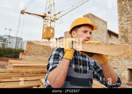 Trasporto di tavole di legno. Lavoratori edili in uniforme e attrezzature di sicurezza hanno lavoro in costruzione Foto Stock