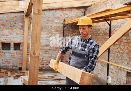 Trasporto di tavole di legno. Lavoratori edili in uniforme e attrezzature di sicurezza hanno lavoro in costruzione Foto Stock