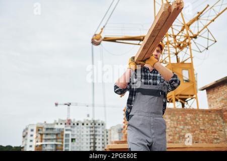 Trasporto di tavole di legno. Lavoratori edili in uniforme e attrezzature di sicurezza hanno lavoro in costruzione Foto Stock