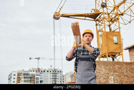 Trasporto di tavole di legno. Lavoratori edili in uniforme e attrezzature di sicurezza hanno lavoro in costruzione Foto Stock