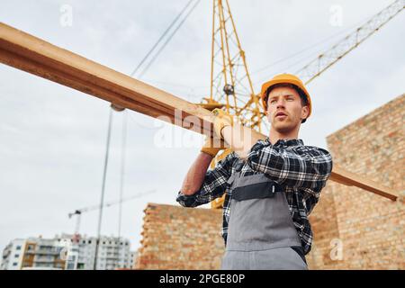 Trasporto di tavole di legno. Lavoratori edili in uniforme e attrezzature di sicurezza hanno lavoro in costruzione Foto Stock