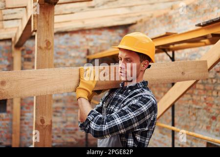 Trasporto di tavole di legno. Lavoratori edili in uniforme e attrezzature di sicurezza hanno lavoro in costruzione Foto Stock