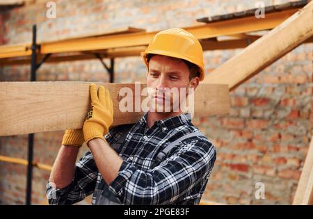 Trasporto di tavole di legno. Lavoratori edili in uniforme e attrezzature di sicurezza hanno lavoro in costruzione Foto Stock