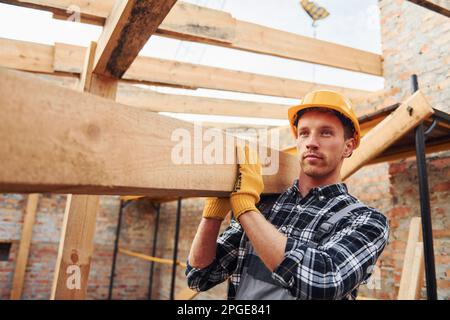 Trasporto di tavole di legno. Lavoratori edili in uniforme e attrezzature di sicurezza hanno lavoro in costruzione Foto Stock