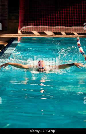 L'atleta nuota in piscina in un cappello e bicchieri, emergendo fa un fungo con le mani, stile farfalla Foto Stock