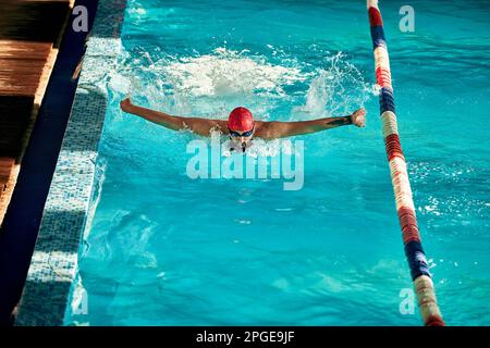 L'atleta nuota in piscina in un cappello e bicchieri, emergendo fa un fungo con le mani, stile farfalla Foto Stock